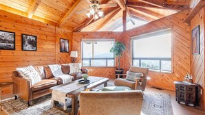 Een gezellig houten cabin interieur met een bank, fauteuils, een salontafel en een groot raam met uitzicht.
