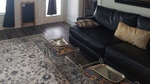 Un salon avec un canapé en cuir noir, un tapis à motifs, une horloge et un tableau accroché au mur.