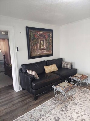 A living room with a black leather sofa, a patterned rug, and a framed painting on the wall. - The Vintage Pearl in Downtown Cleveland (Cleveland)