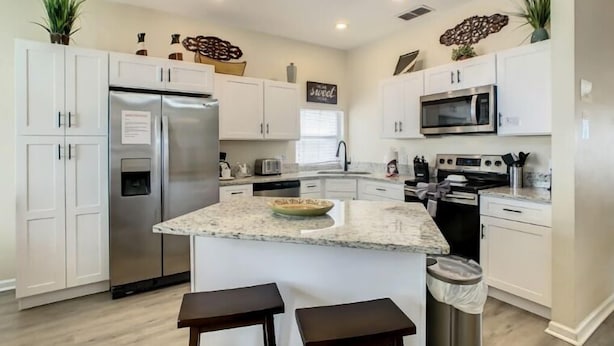 A modern kitchen with white cabinets, stainless steel appliances, and a granite countertop. - Resort-Style Villa | Pool, Spa & Game Room! (Kissimmee)