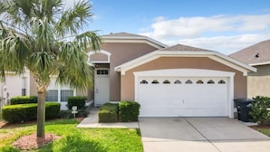 A residential house with a white garage, a palm tree, and well-maintained lawn. - Resort-Style Villa | Pool, Spa & Game Room! (Kissimmee)