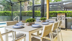 A covered patio with a dining table set for four, surrounded by chairs. There is a grill and a pool visible in the background. - 5Br Davenport Home W/ Pool & Private Hot Tub (Davenport)
