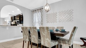 A dining area with a rectangular table, six patterned chairs, a chandelier, and decorative wall art. - 5Br Davenport Home W/ Pool & Private Hot Tub (Davenport)