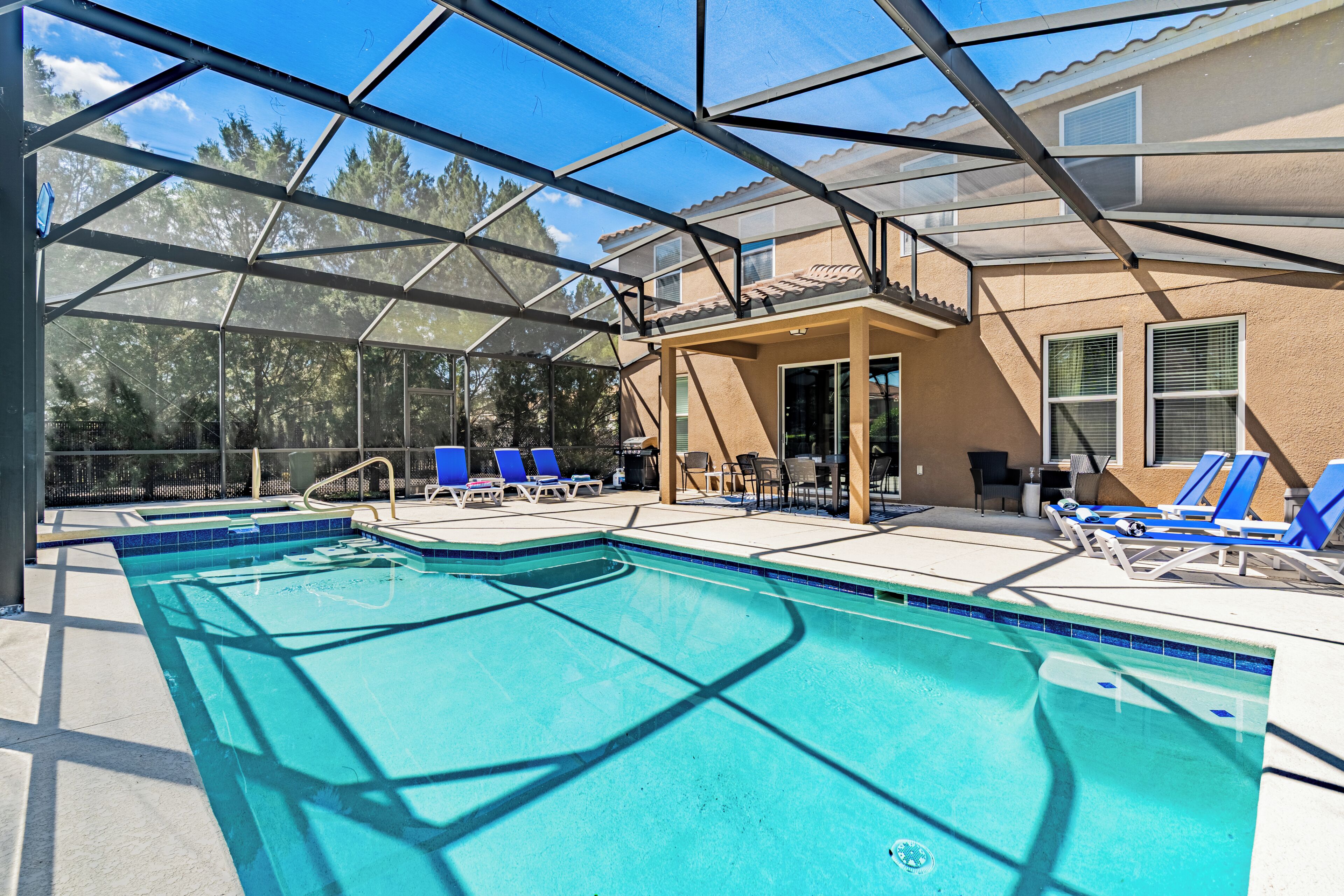 A swimming pool with blue tiles, surrounded by lounge chairs and a covered patio area.