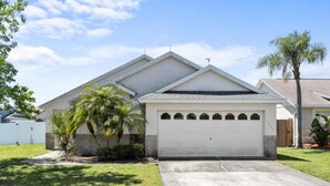 A single-story house with a garage, a front lawn, and a palm tree. - Sunny Private Pool & Spa & Fenced Yard. Nr Parks (Kissimmee)