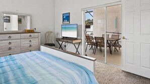 A bedroom with a bed, a desk with a computer, a chair, and a sliding glass door leading to a balcony with outdoor seating. - Sunny Private Pool & Spa & Fenced Yard. Nr Parks (Kissimmee)
