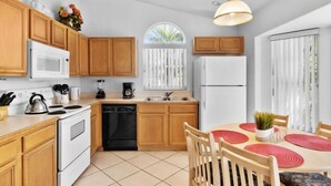 A modern kitchen with wooden cabinets, white appliances, and a dining area with a table and chairs. - Sunny Private Pool & Spa & Fenced Yard. Nr Parks (Kissimmee)