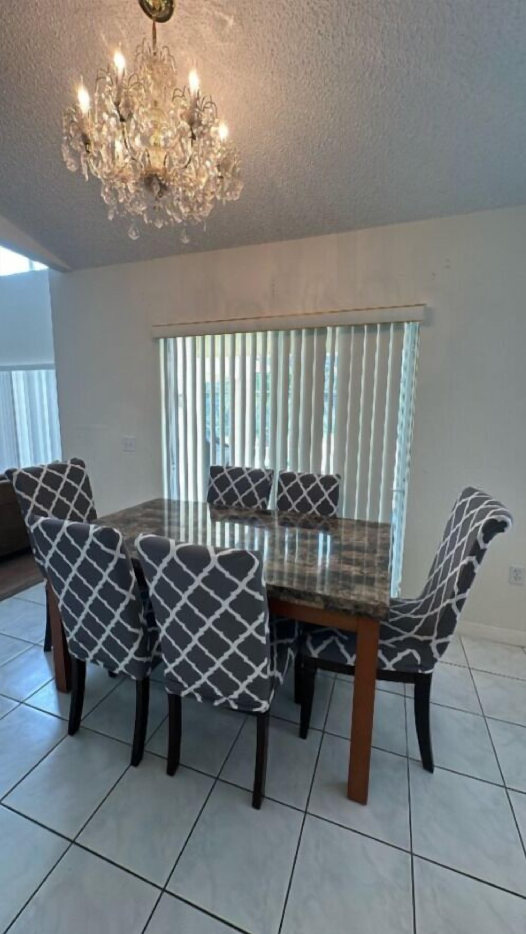 A dining area with a chandelier, a table, chairs, and a window with blinds.