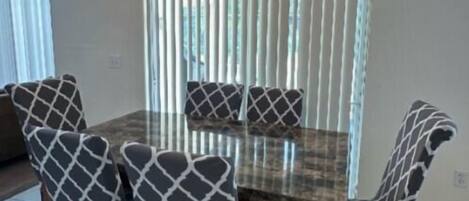 A dining area with a chandelier, a table, chairs, and a window with blinds.