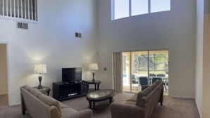 A spacious living room with a large window, a flat-screen TV, and a sliding glass door leading to an outdoor area. - South Facing W/ Private Pool & Spa (Kissimmee)