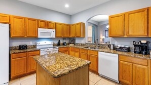A modern kitchen with wooden cabinets, granite countertops, a central island, and stainless steel appliances. - Relax & Unwind – Stunning Home W/ Private Pool! (Kissimmee)