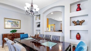 A dining area with a wooden table, blue upholstered chairs, and decorative items on shelves. - Relax & Unwind – Stunning Home W/ Private Pool! (Kissimmee)