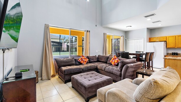 A modern living room with a sectional sofa, ottoman, and a dining area with a table and chairs. - Relax & Unwind – Stunning Home W/ Private Pool! (Kissimmee)