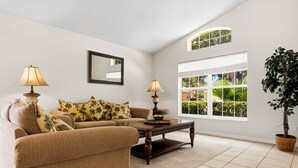 A living room with a sofa, two lamps, a coffee table, a mirror, and a window with blinds. - Emerald Island Retreat Near Parks (Kissimmee)