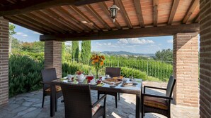 Un patio al aire libre con una mesa dispuesta para una comida, rodeado de pilares de ladrillo y una pérgola.