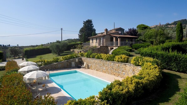 Una casa de piedra con piscina, rodeada de exuberante vegetación y un cielo despejado.