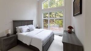 Un dormitorio con una ventana grande, una cama, una mesita de noche y un aparador.