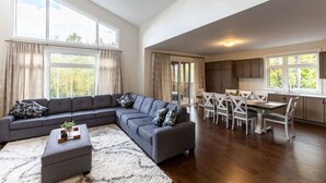 Amplia sala de estar con sofá seccional gris, una mesa de comedor con sillas y una cocina con armarios y ventana.