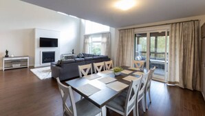 Una sala de estar moderna con sofá, televisor, chimenea, mesa de comedor y ventanas grandes.