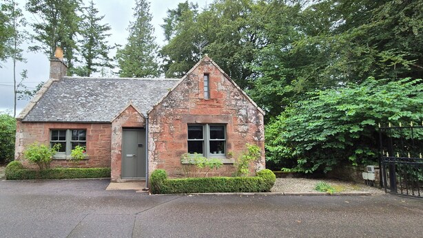 A small, single-story stone building with a steeply pitched roof, a chimney, and a small porch area. - Gate Lodge - historic rural cottage with hot tub, Aberdeenshire (Fettercairn)