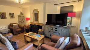 A living room with a sofa, armchairs, a coffee table, a television, and a cabinet. - Gate Lodge - historic rural cottage with hot tub, Aberdeenshire (Fettercairn)