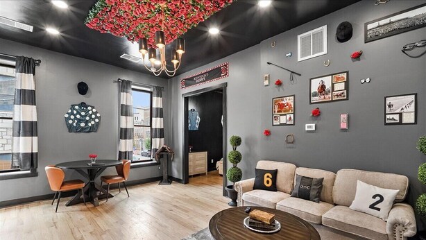 A modern living room with a round coffee table, a sofa with numbered cushions, a dining area with striped curtains, and a chandelier with red flowers. - Off to the Races Retreat - Hidden Clues Inside (Frankfort)