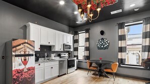 A modern kitchen with white cabinets, a dining area with a round table and chairs, and a large window with striped curtains. - Off to the Races Retreat - Hidden Clues Inside (Frankfort)