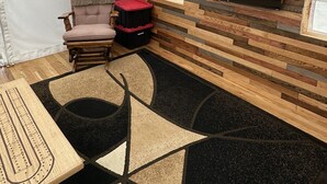 Una habitación con tienda de campaña, televisión, un sillón acolchado, una mesita y una alfombra estampada.