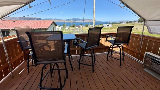Una terraza cubierta al aire libre con una mesa y sillas, con vistas a un paisaje pintoresco que incluye montañas y una masa de agua.
