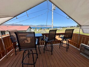 A covered outdoor deck with a table and chairs, overlooking a scenic landscape with mountains and a body of water.
