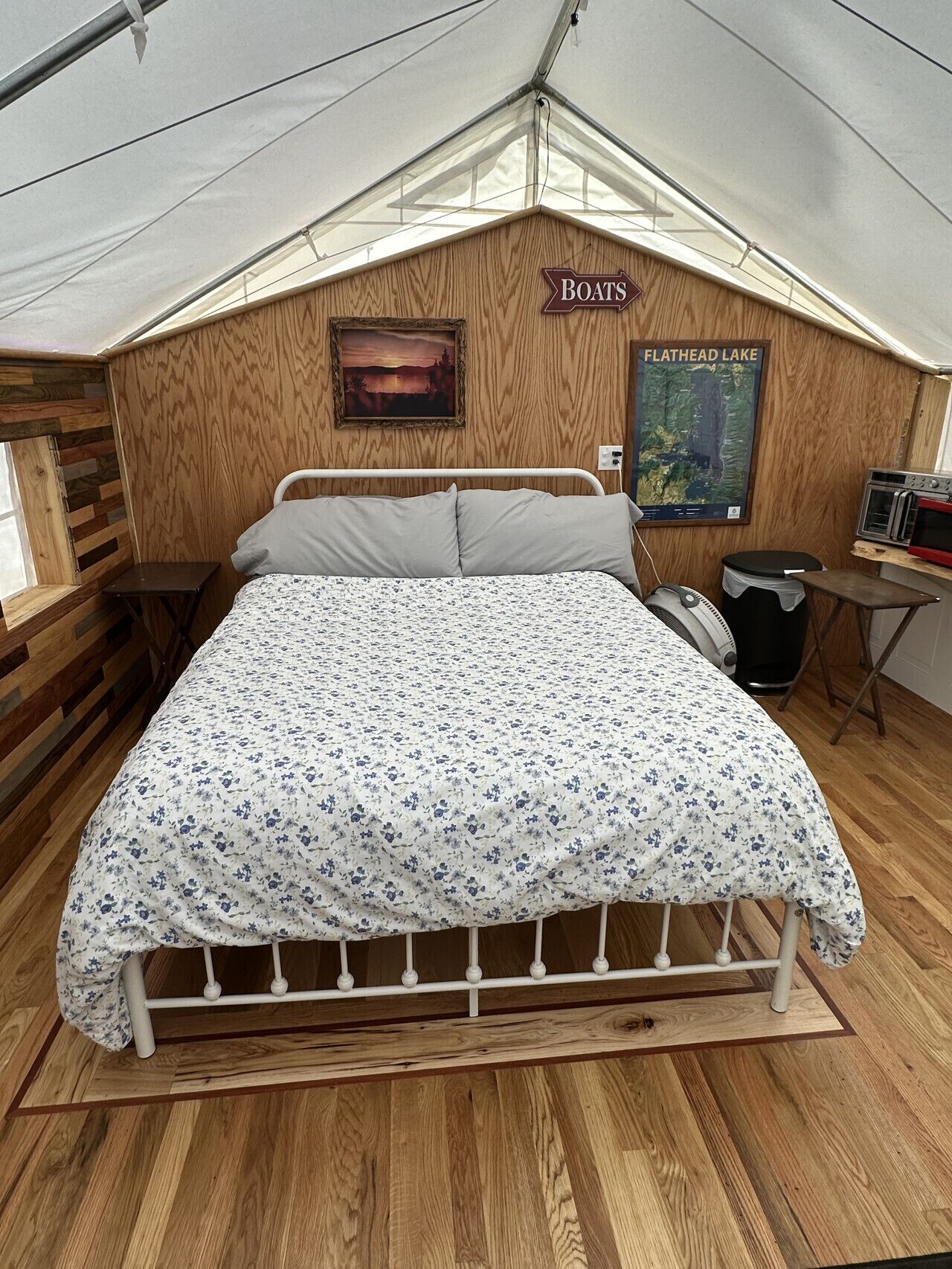 Quarto com beliche de madeira, uma cama de solteiro com colcha florida, TV fixada na parede, pôster do Lago Flathead e placa indicando que o quarto é para barcos.