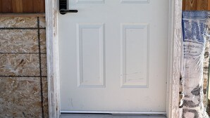 Una puerta blanca con un letrero que dice “BATHHOUSE” encima, un teclado de combinación y una pared de madera con superficie texturizada.
