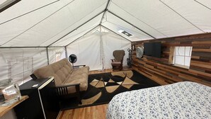 Una habitación con carpa, una cama, una silla, un escritorio y un ventilador.