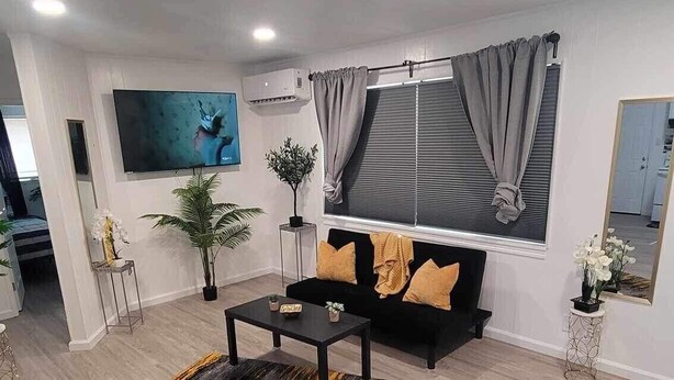 A modern living room with a black sofa, a coffee table, and a large window with curtains. - The Hideaway (Sacramento)
