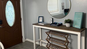 Een hal met een houten console tafel, een spiegel, een ingelijste foto, een bord en een plek voor huisdierenvoer.