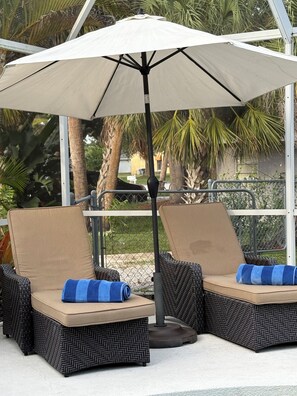 Two lounge chairs with cushions, an umbrella, and a metal fence in the background. - Venice FL 3BR Home • Private Pool • 1925 Historic • Near Beach (Venice)