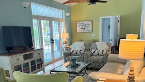 A living room with a TV, green armchairs, a patterned sofa, and a ceiling fan. - Renovated 1925 Bungalow • Heated Pool • 3BR En-Suite • 2 Mi to Venice Beach (Venice)