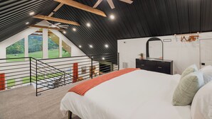 A bedroom with a large bed, a black dresser, a ceiling fan, and a view of a green landscape through a window. - BRAND NEW Mountain Barndominium Retreat / Sleeps 6 / 4 Miles to Main St (Waynesville)