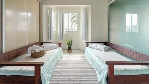 Una habitación con dos camas, una cesta de mimbre, una planta en maceta y vistas a palmeras a través de la ventana.