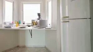 Una pequeña cocina con un refrigerador blanco, una cafetera y diferentes utensilios de cocina sobre la encimera.