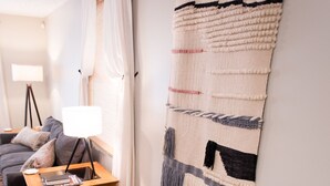 A cozy living room with a wooden bench, a small table with a lamp, and a large woven tapestry on the wall.