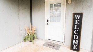 A white door with a window, a welcome sign, a potted plant, and a doormat.