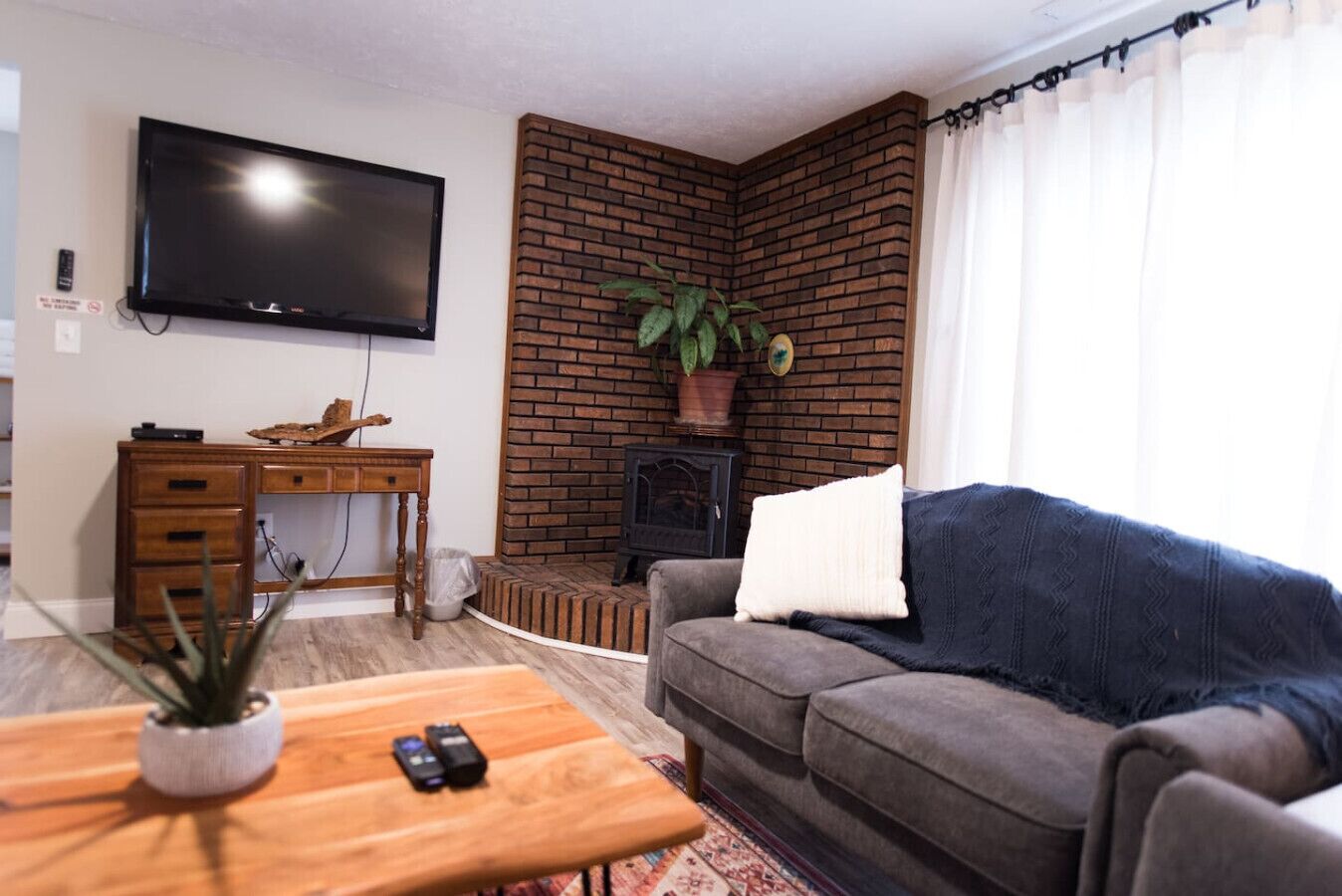 Een woonkamer met een televisie, een bakstenen muur, een bank, een salontafel en een bureau.