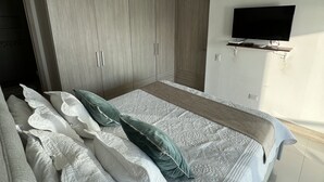 Een slaapkamer met een bed, een aan de muur bevestigde televisie en een kledingkast.