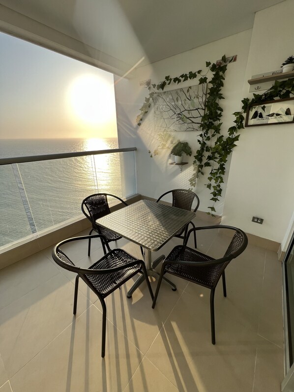 Un balcon avec une table et des chaises, une vue sur la mer et des plantes décoratives.