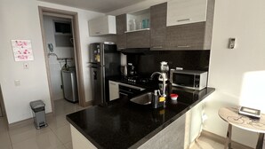 Een moderne keuken met een centraal eiland, roestvrijstalen apparatuur en een kleine eethoek met een tafel en stoelen.
