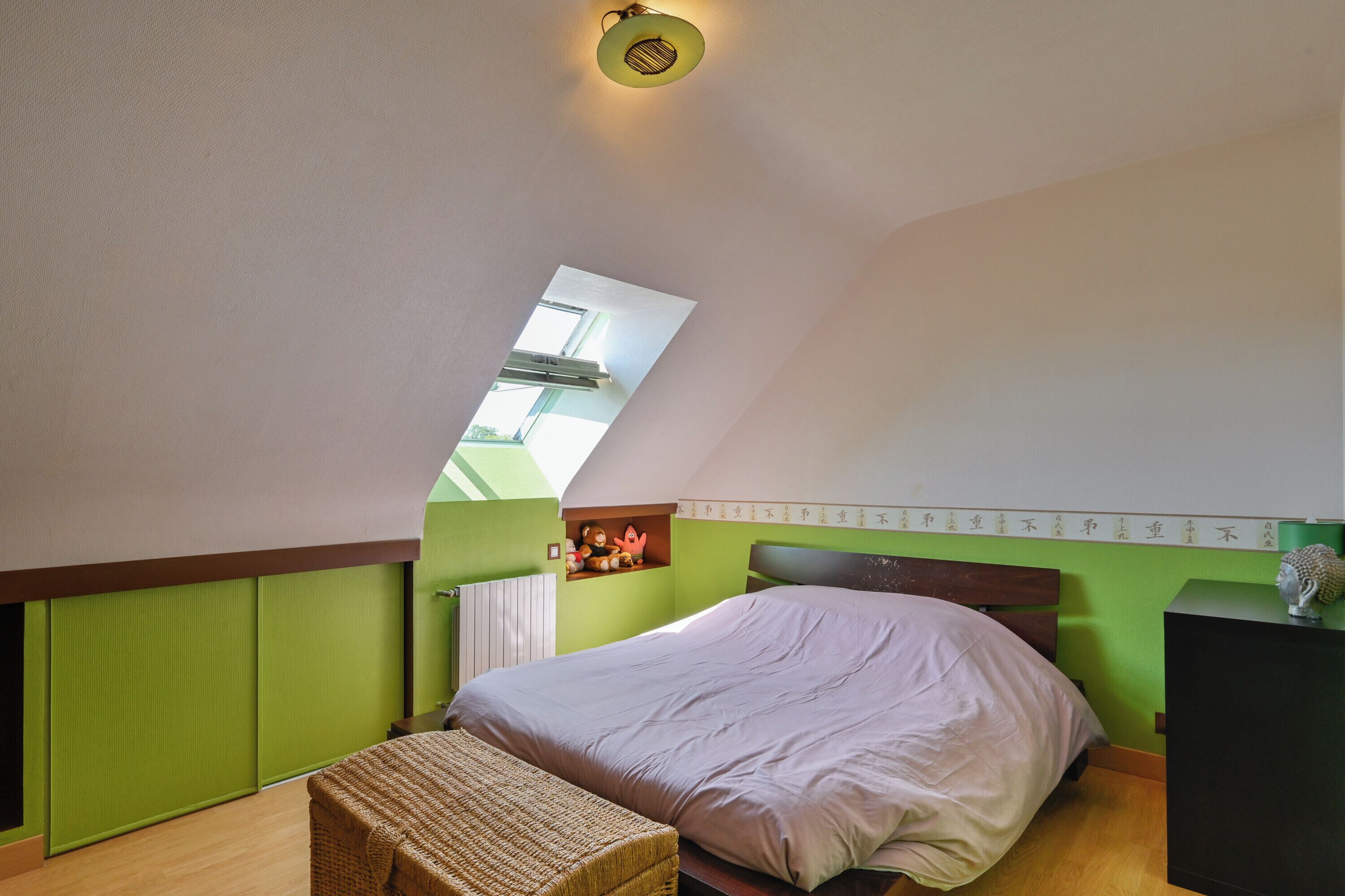 A bedroom with a sloped ceiling, a skylight, a bed, a small table, and a dresser.