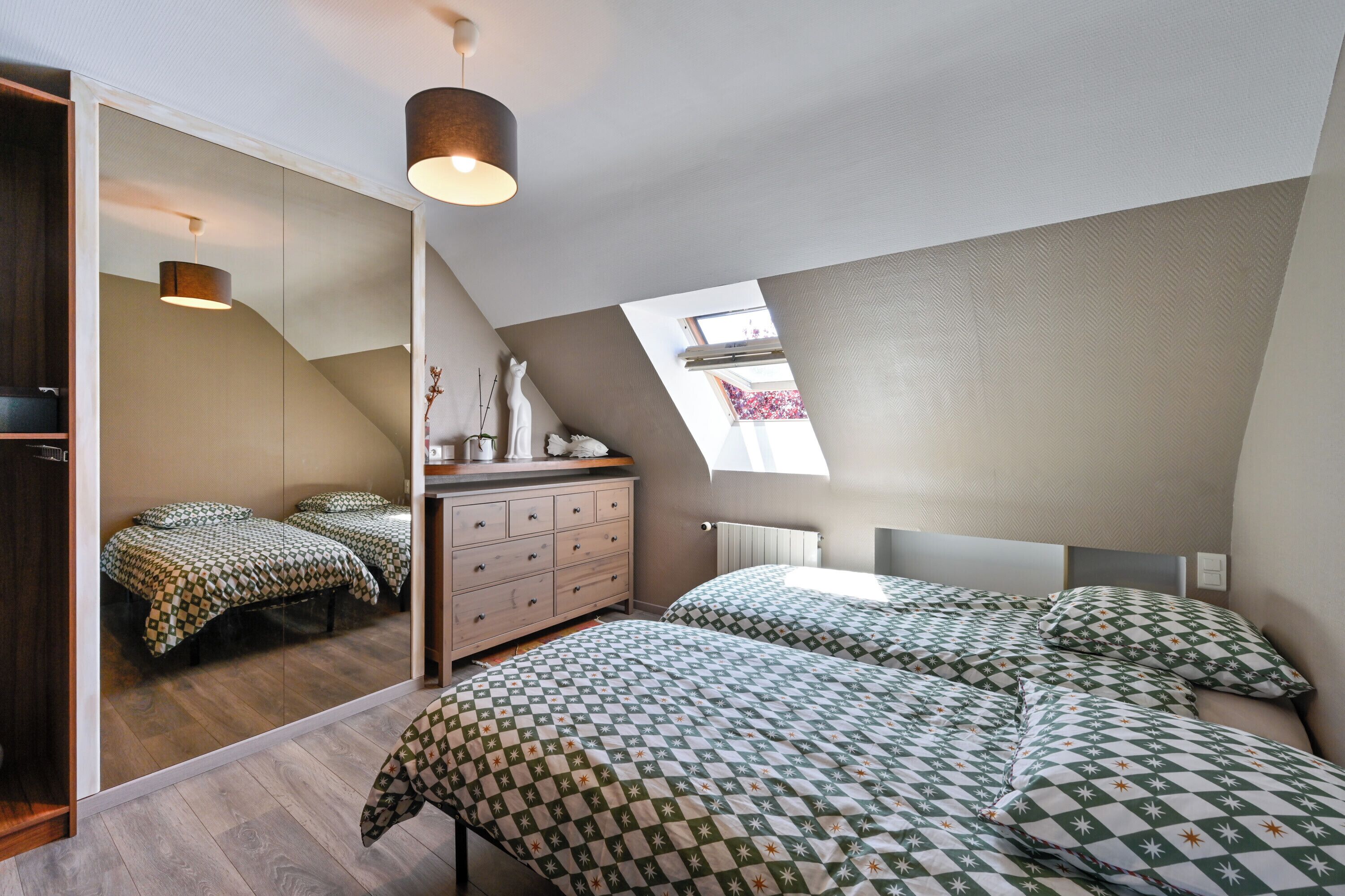 A bedroom with two beds, a dresser, a mirror, and a skylight.