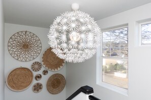 A room with a white ceiling, a large window, and various wall decorations including woven baskets and geometric patterns.