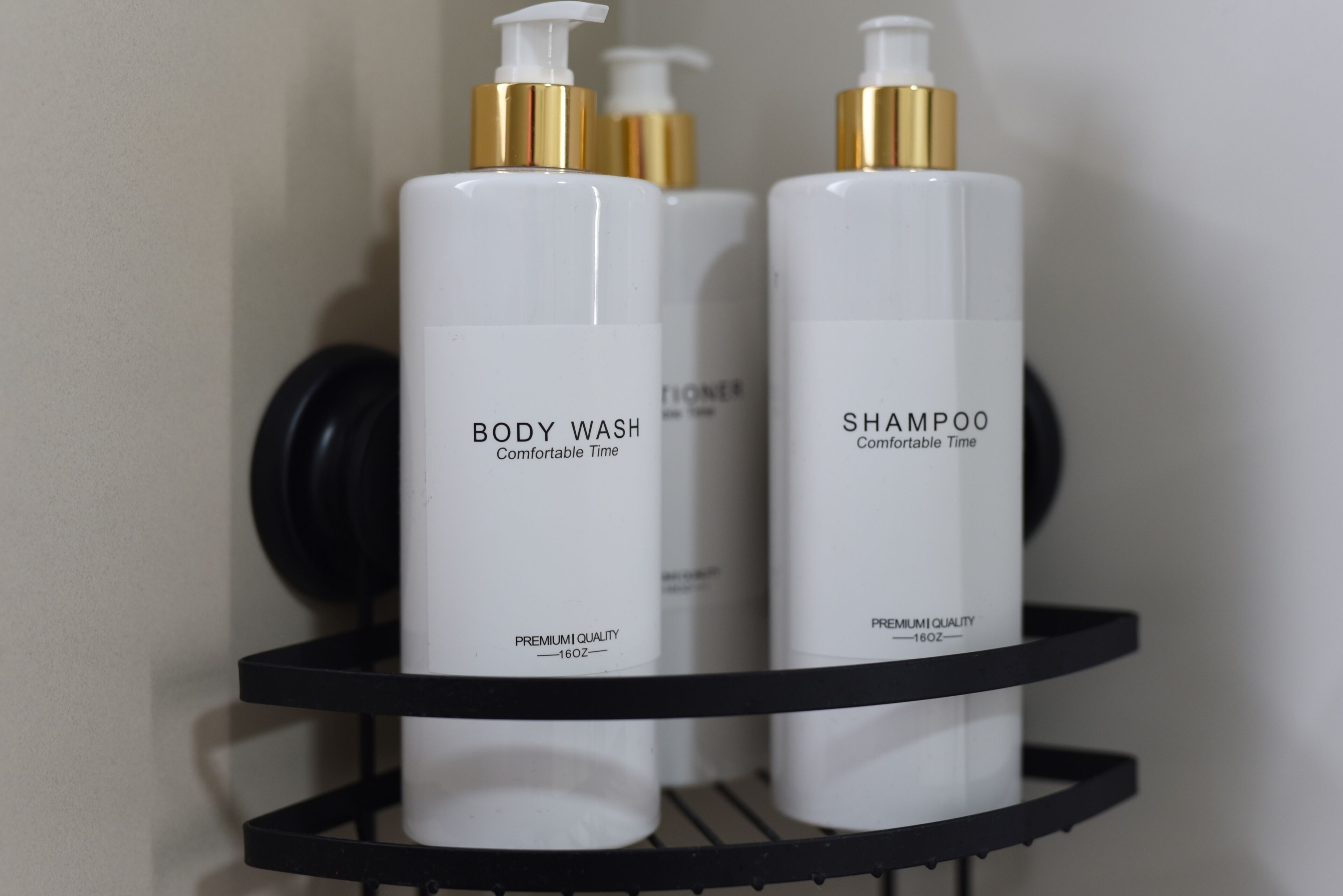 A black metal shelf with three white bottles labeled 'BODY WASH' and 'SHAMPOO' on a wall.